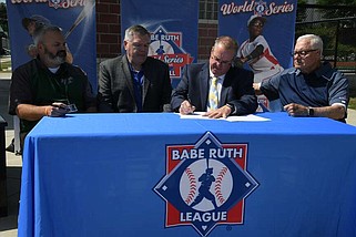 Babe Ruth League Vice President of Operations Rob Connor, middle, signs the contract for Majestic Park to host the 2025 Babe Ruth World Series on Wednesday. (The Sentinel-Record/Lance Brownfield)